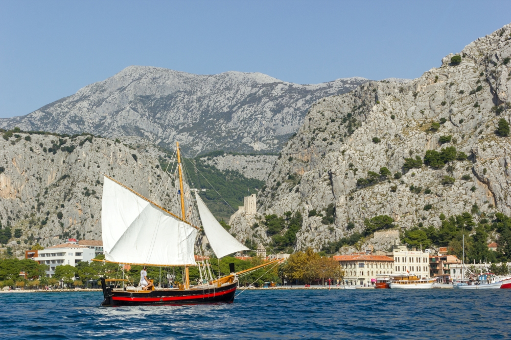 A traditional wooden sailing ship, a Jedrenjak, passing by Omiš Old Town on the Cetina river